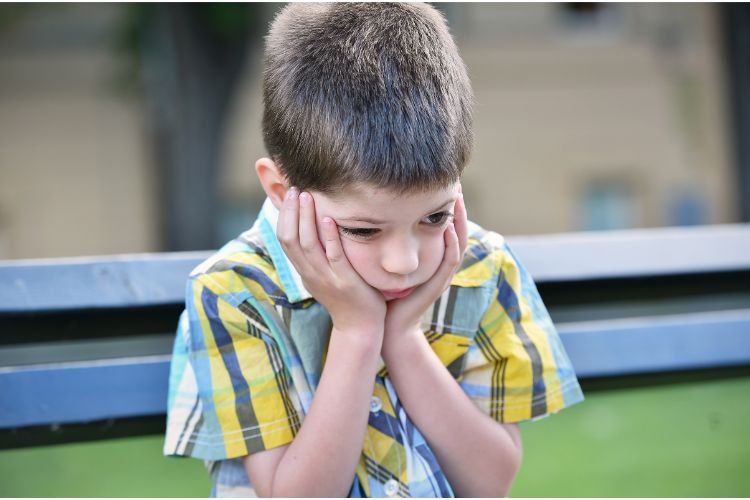 Child sitting alone on playground, potential sign of social bullying